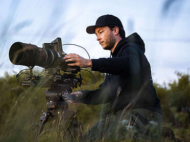 Ein junger Mann mit einer Filmkamera in den Dünen