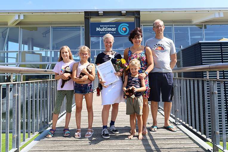 Drei Erwachsene und drei Kinder stehen vor dem Haupteingang vom Multimar Wattforum, mit einer Urkunde und einem Blumenstrauß in den der hand