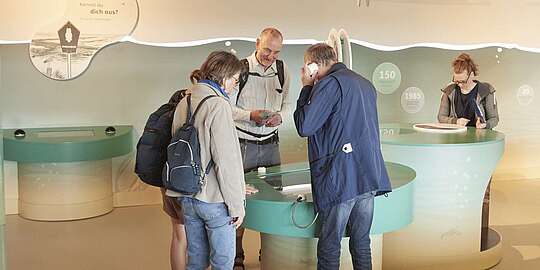 Eine Gruppe Erwachsener beugt sich über die Ausstellung im Multimar Wattforum