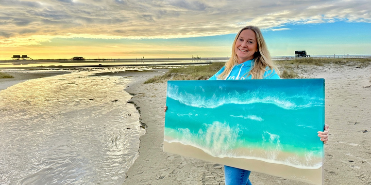 Eine Frau steht am Strand von St. Peter-Ording mit einem Bild in den Händen