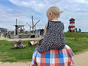 Kind sitz auf den Schulter eines Erwachsenen und blickt auf einen Spielplatz