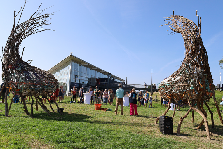 Mehrere Menschen stehem um zwei meterhohe Skulpturen aus Zweigen herum